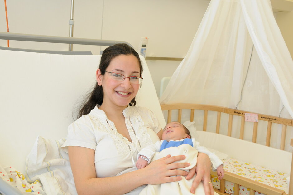 Eine junge Mutter sitzt mit ihrem Neugeborenen im Arm in der einem Krankenbett auf der Wochensation in Greifswald.